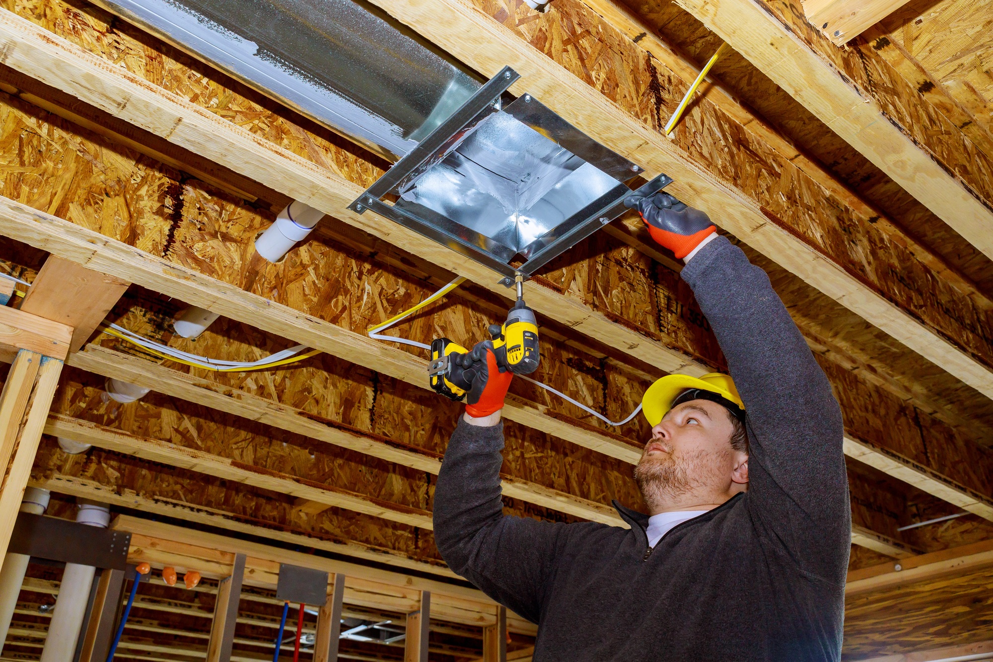 Male technician mounted air heating and cooling system on ceiling steel roof structure ventilation